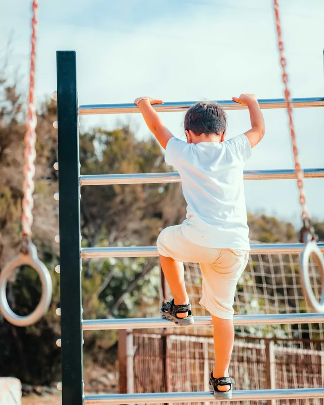 Un enfant de dos qui grimpe une échelle de parc, au soleil (photo d'ambiance)