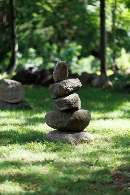 Des pierres empilées les unes sur les autres, dans l'herbe d'un sous-bois (photo d'ambiance)