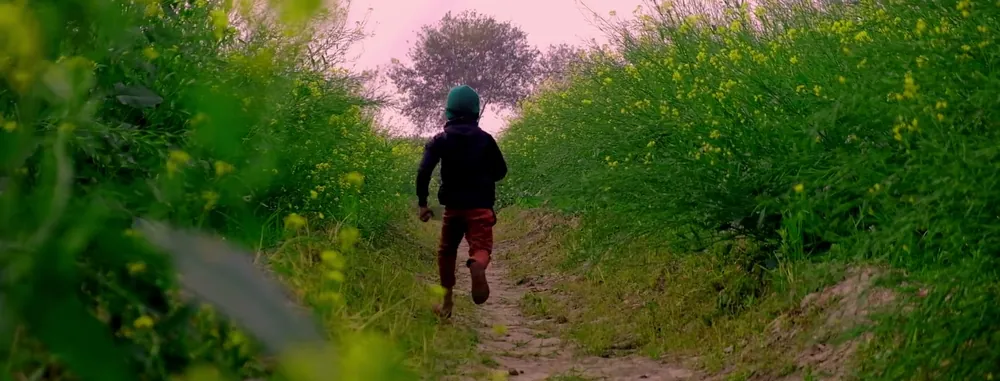 Un enfant de dos qui court au loin sur un sentier entre les champs (photo d'ambiance)