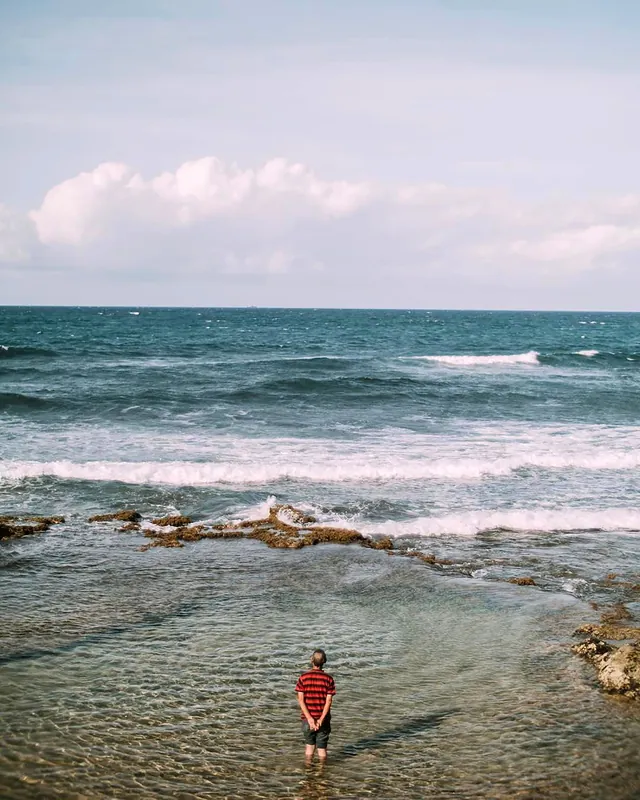 Un enfant de dos, debout dans l'eau, qui regarde les vagues arriver (photo d'ambiance)