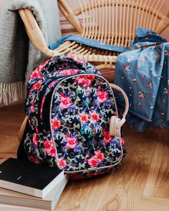 Un sac d'école fleuri posé par terre, à la maison, près d'une chaise et de quelques livres (photo d'ambiance)