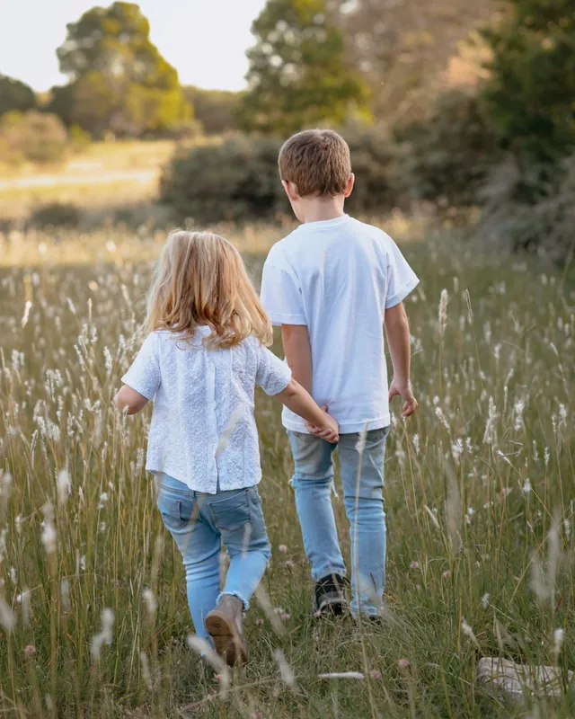 Un frère et une sœur, de dos, qui marchent côte à côte dans les herbes hautes (photo d'ambiance)