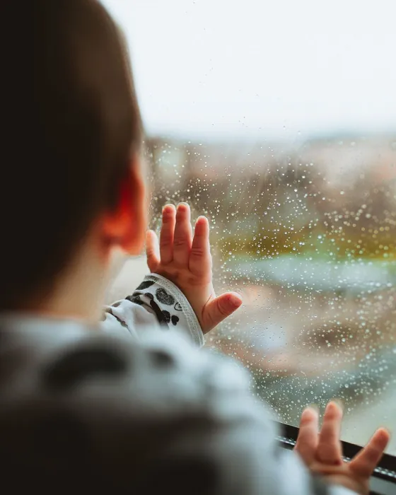 Les mains d'un enfant posées sur une fenêtre mouillée de pluie (photo d'ambiance)