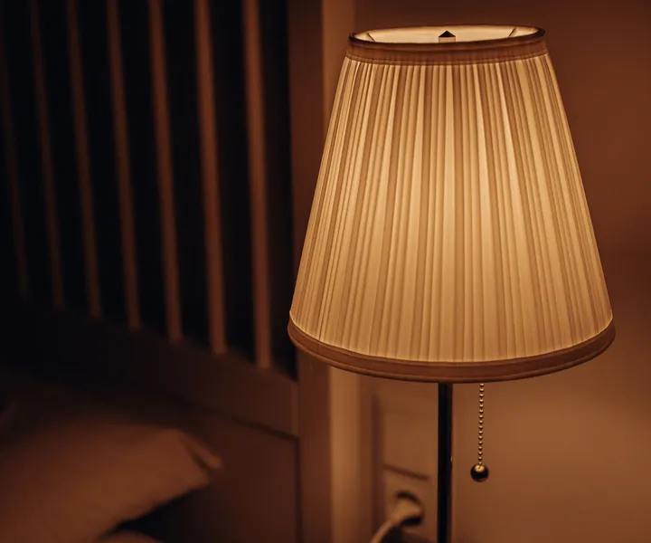 Image d'ambiance : une lampe allumée dans une chambre sombre, près d'un oreiller