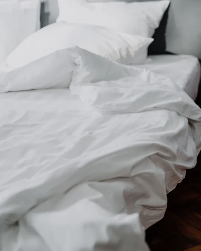 Image d'ambiance : un lit aux draps blancs, la couette qui glisse vers le plancher