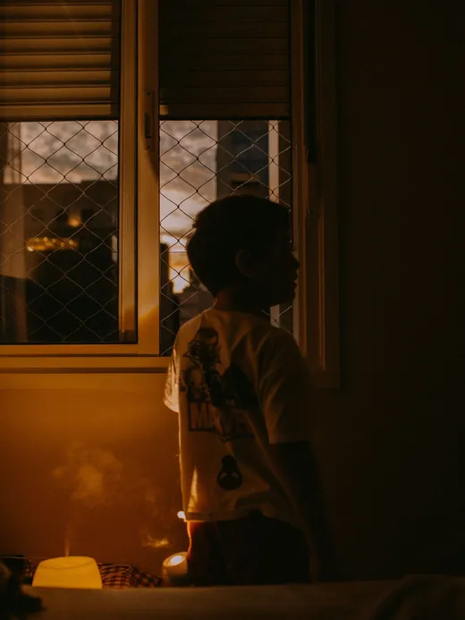Image d'ambiance : un enfant en silhouette près de sa fenêtre et d'une veilleuse, le soir