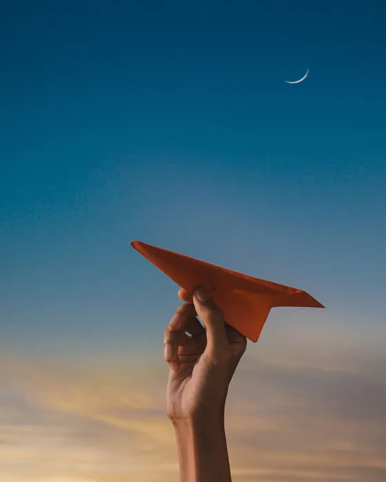 Image d'ambiance : une main qui lance un avion de papier dans le ciel du soir