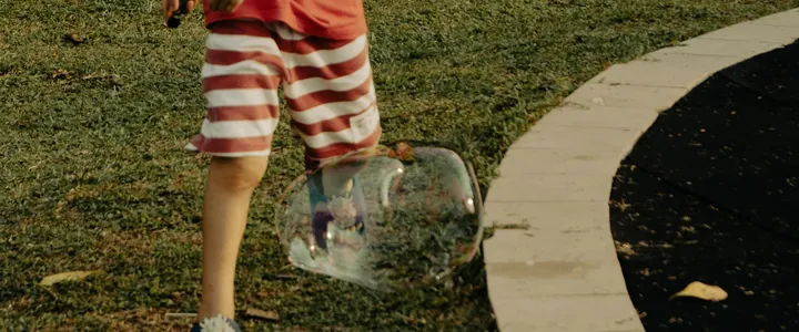 Image d'ambiance : un enfant qui joue avec une bulle de savon dans l'herbe