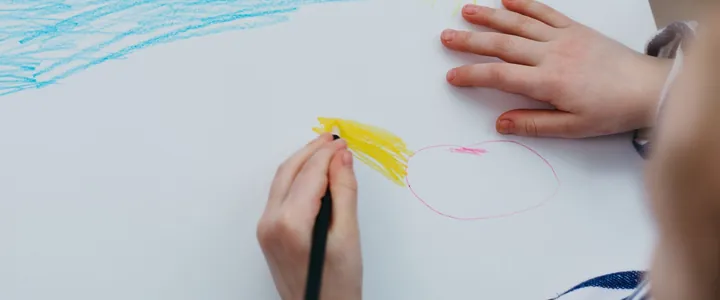 Image d'ambiance : une main d'enfant qui dessine un soleil aux crayons