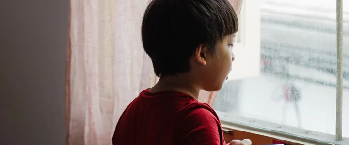 Image d'ambiance : un enfant de dos, à la fenêtre, près d'un rideau rose