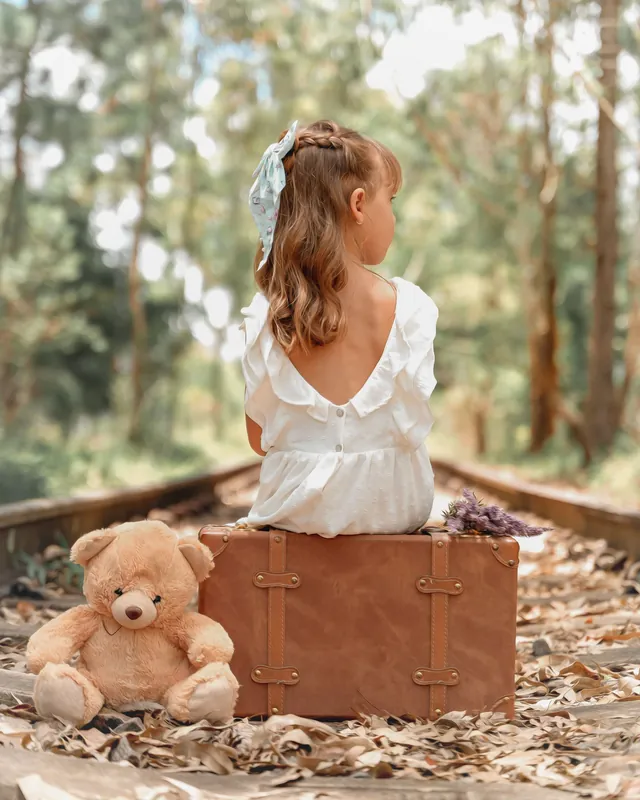 Une fillette de dos, assise sur une valise, son ourson à côté d'elle (photo d'ambiance)